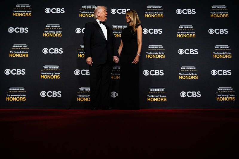 2025年12月7日，美国总统川普与第一夫人梅兰妮亚在「甘迺迪中心荣誉奖」颁奖典礼的红毯拍照背板前留影。背板上清楚可见尚未更名的「甘迺迪中心」与转播单位CBS的标志与字样。（美联社）